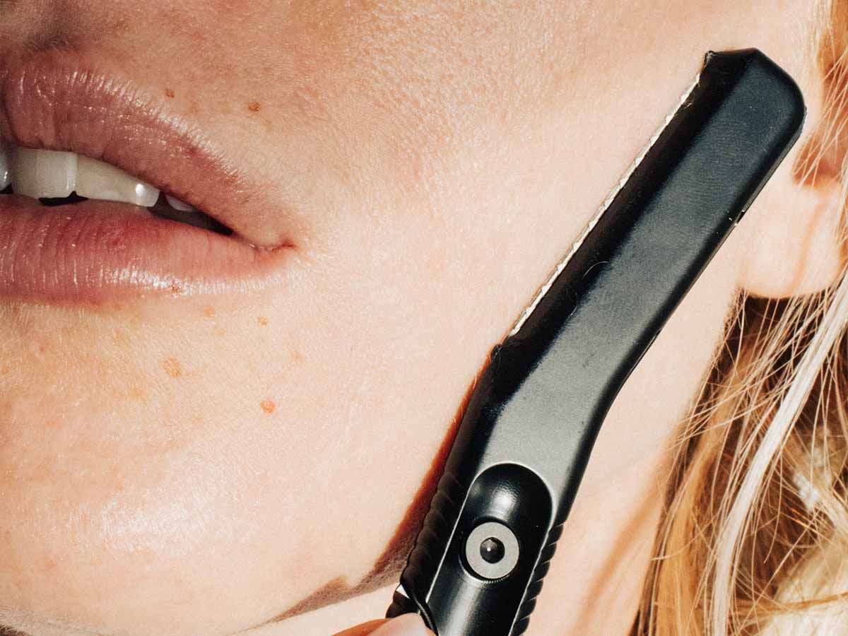 Women holding a black Leaf Dermaplaner against her cheek, closeup