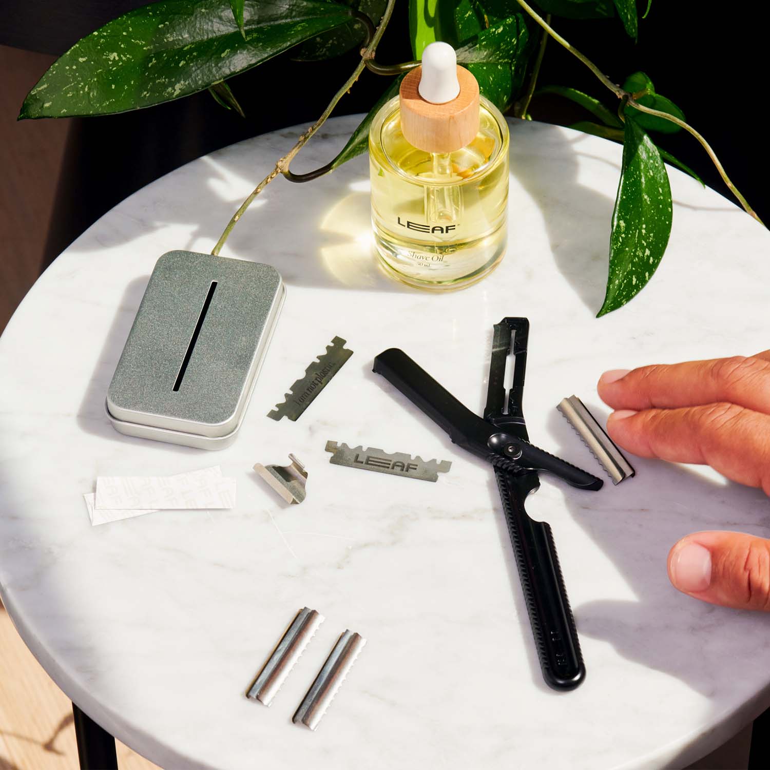 Dermaplaner tool with it's refillable components apart, on a marble table next to shave oil and fresh refillables.