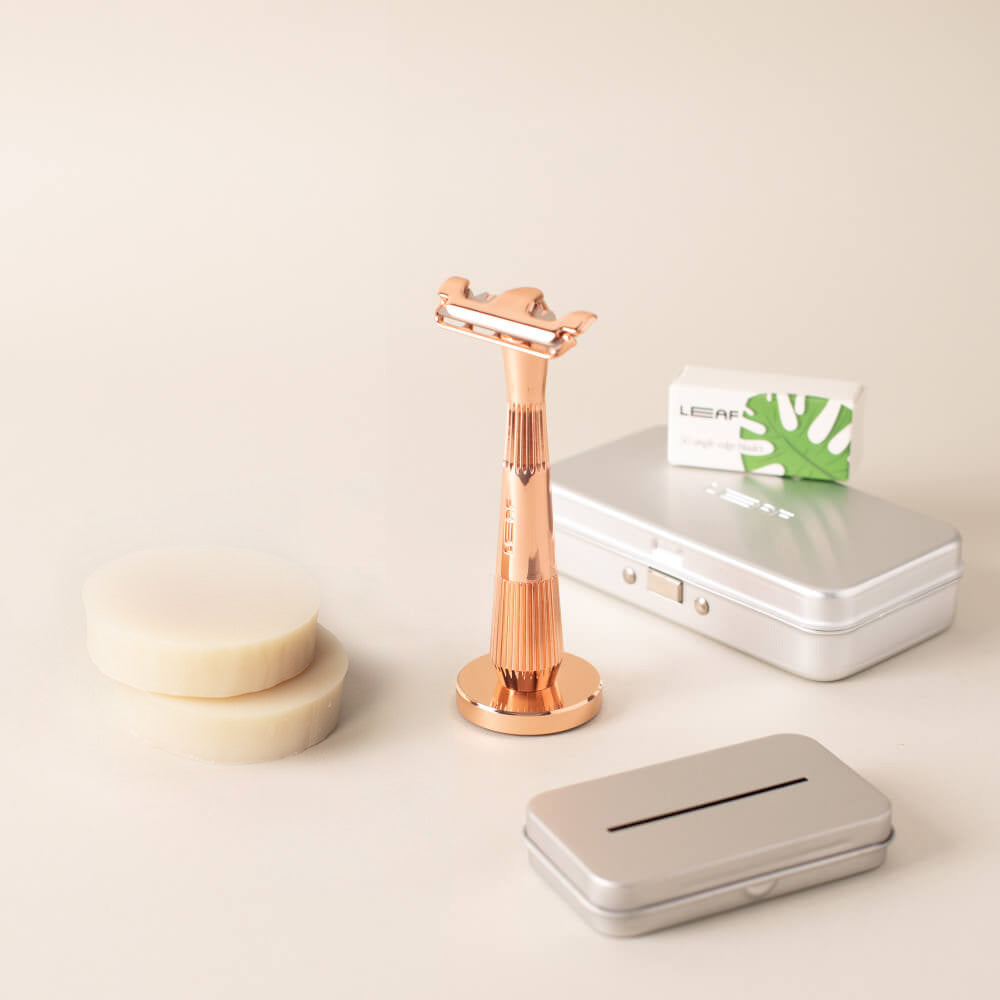 Rose gold single edge razor upright in stand with blade pack, recycling tin, and two off-white shave soaps