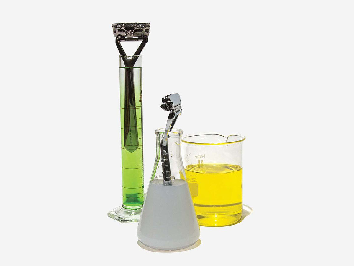 Three beakers with colored liquid in them, and razors