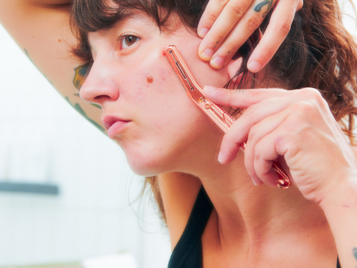 Women dermaplaning her face with a rose gold tool