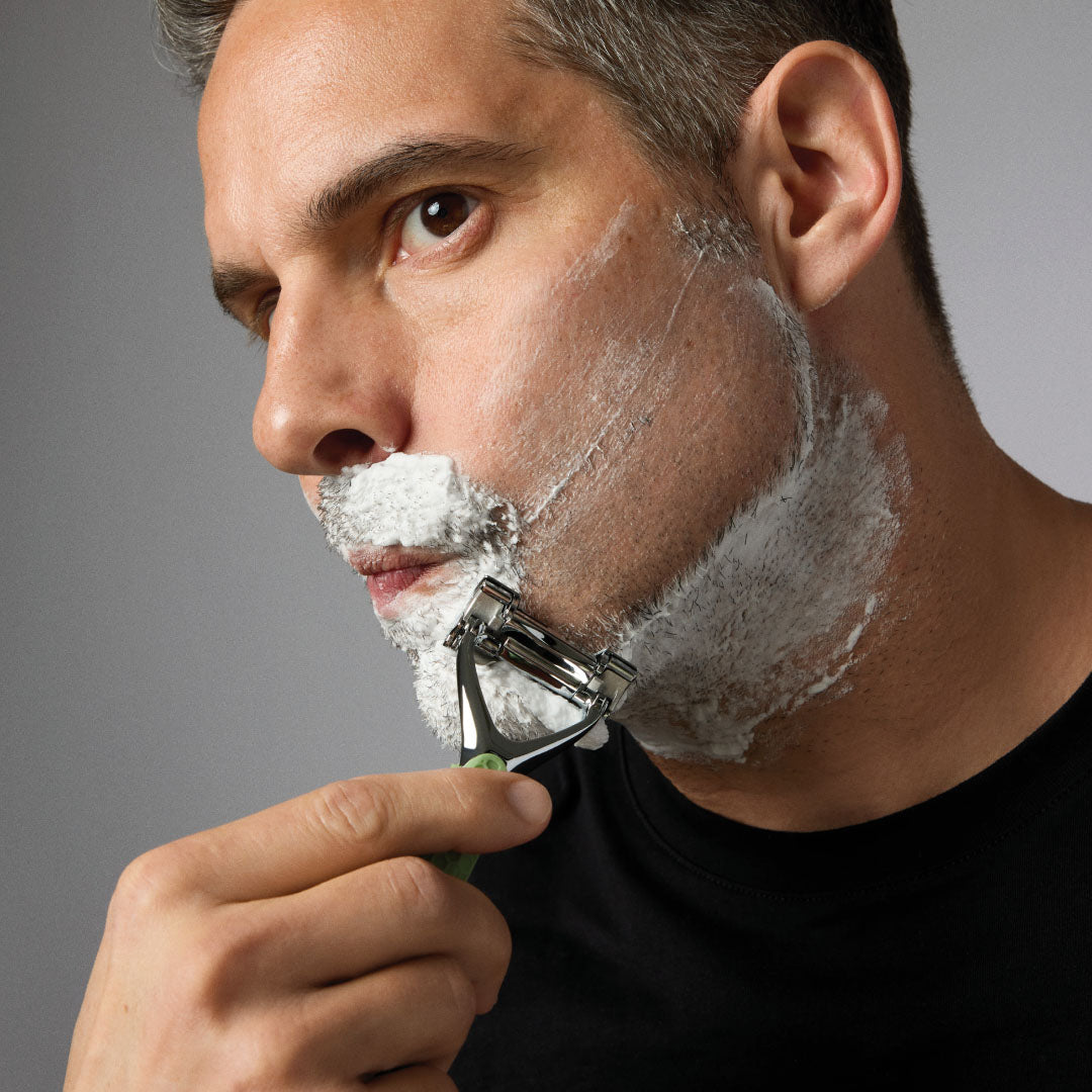 FACE Man shaving his face with a razor on a gray background