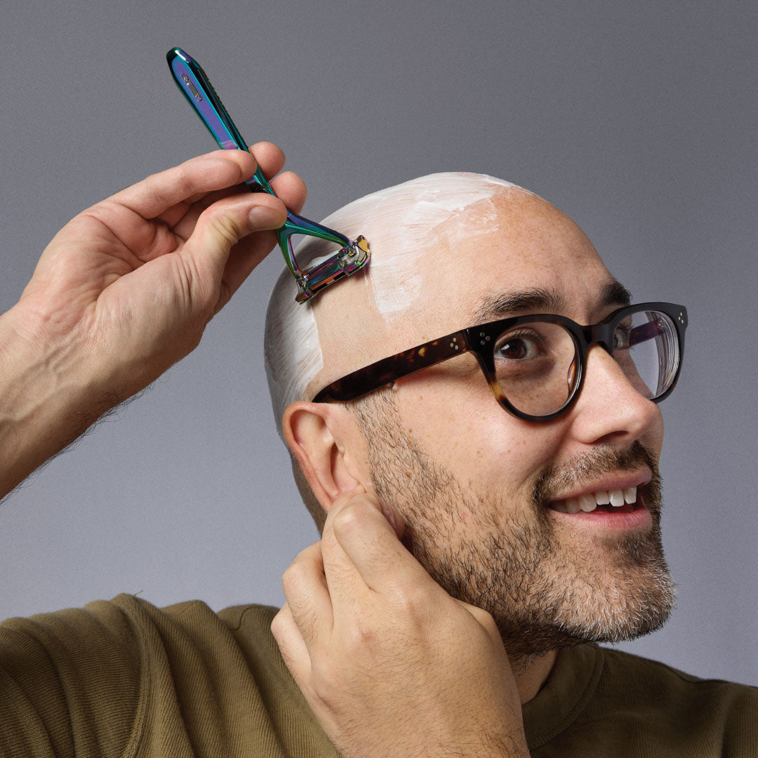 HEAD Man with glasses shaving his head with a razor on a gray background