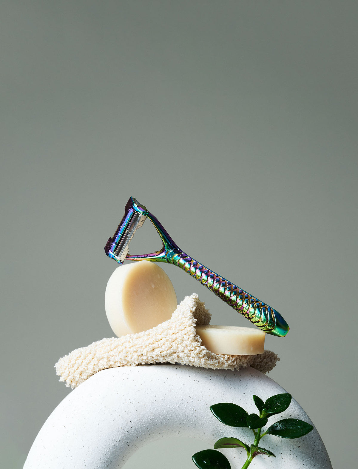 Iridescent razor, soap, and washcloth on a gray background