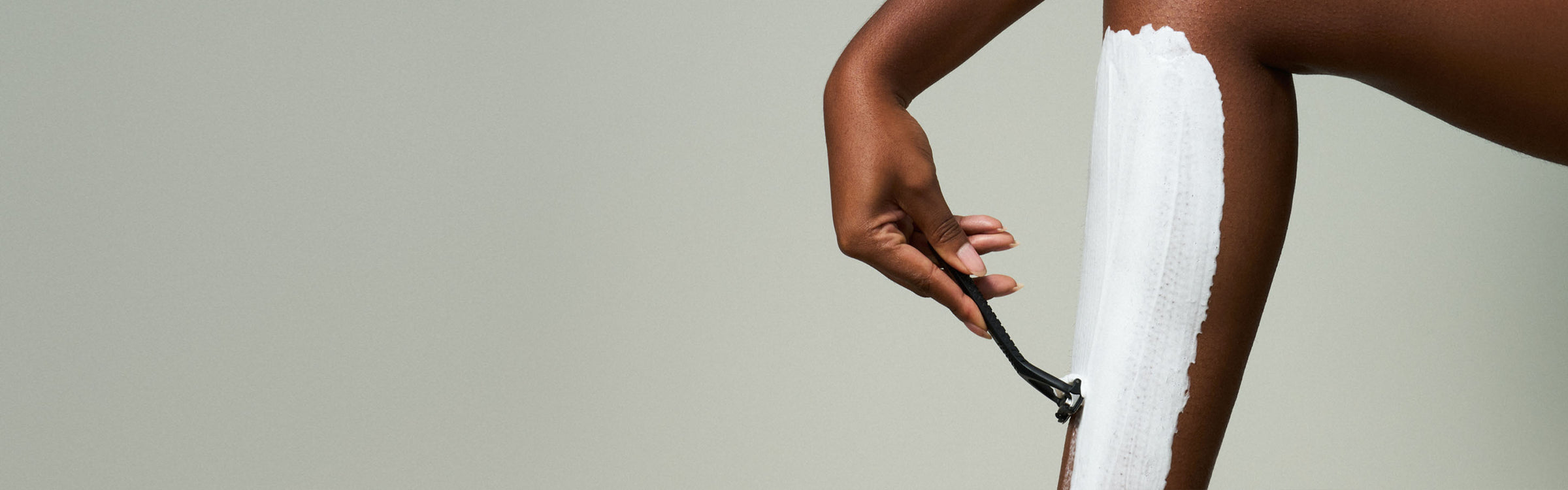 Person applying white cream or lotion to their arm against a neutral background