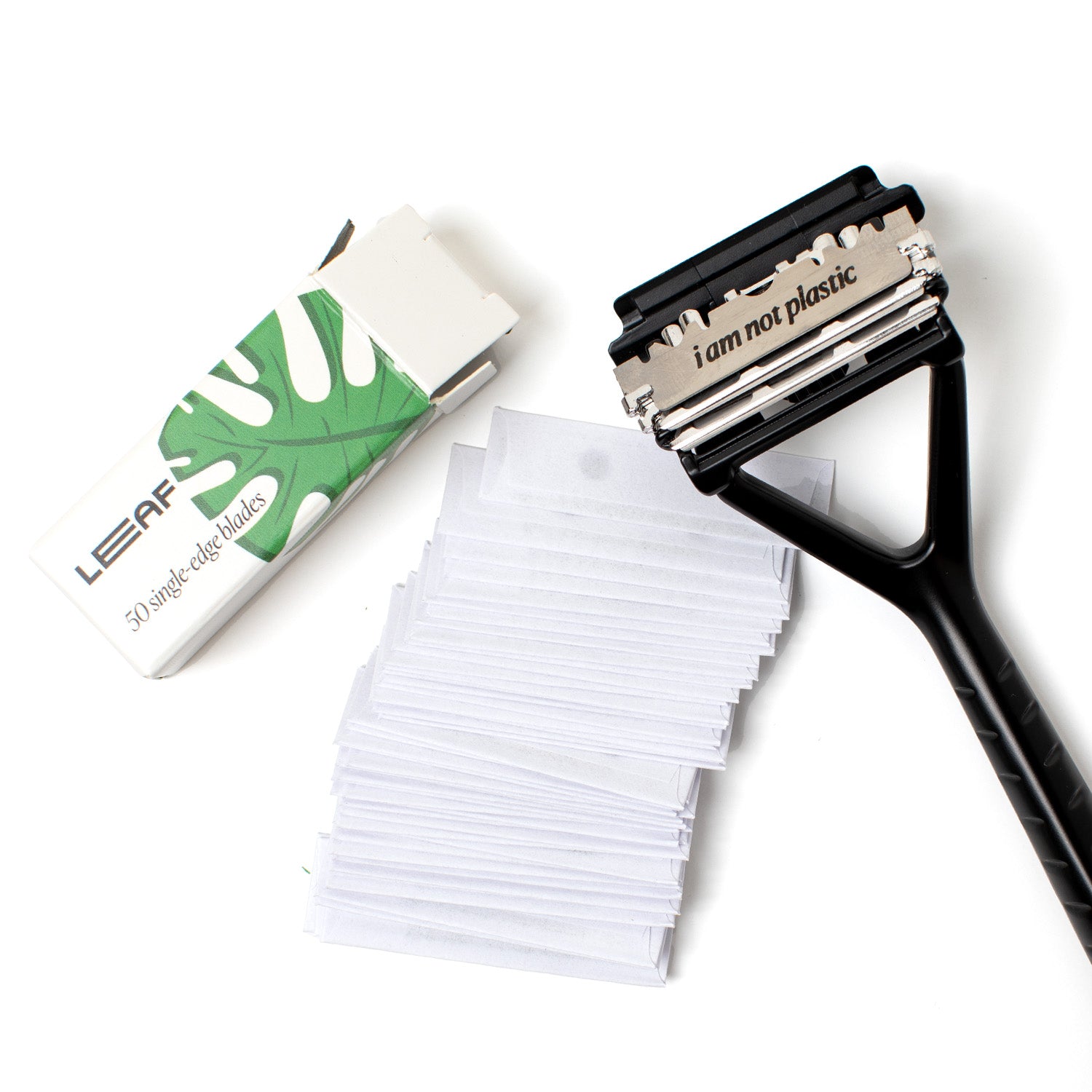 Leaf Razor lying next to pack of 50 blades, with head flipped open and blade visible that reads "I am not plastic"