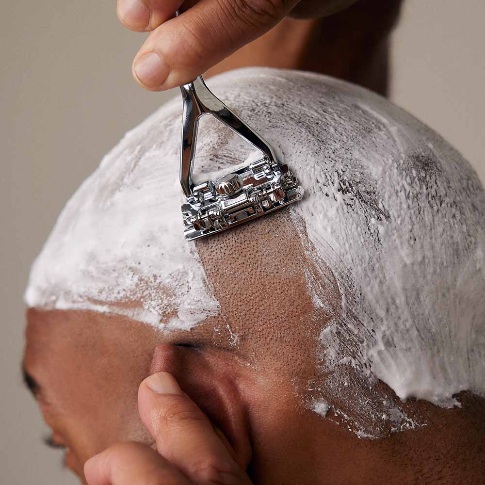 Man shaves his head covered in shave soap with a leaf razor