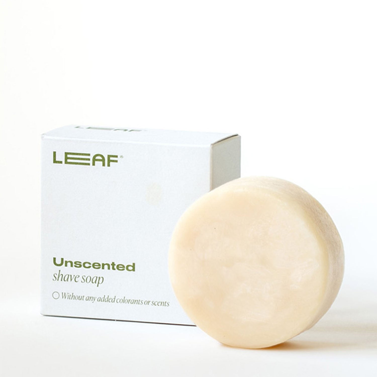 A round bar of shave soap sitting in front of it's Leaf Shave packaging box
