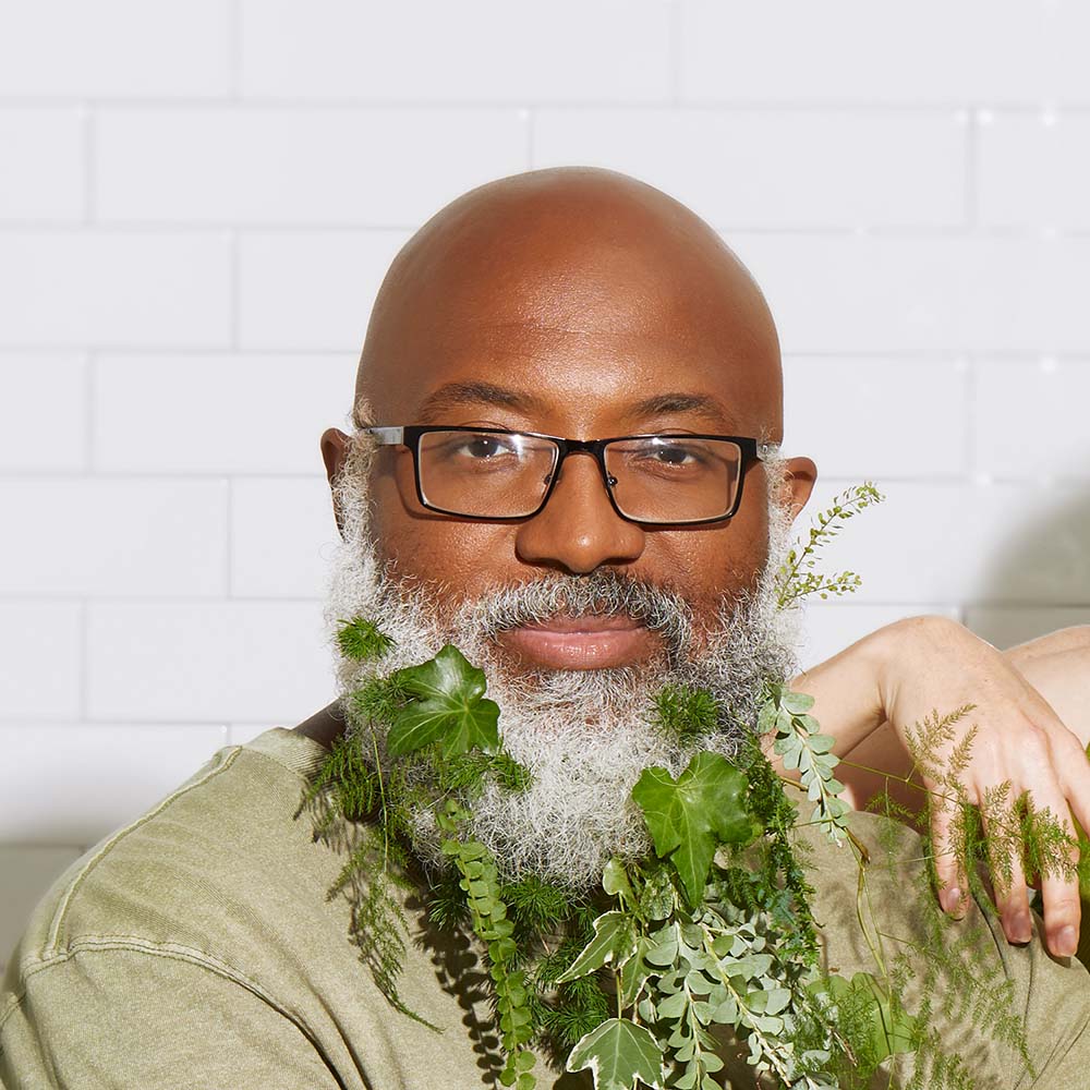 Man with glasses and green leaves threaded throughout his beard, with a clean head shave from his leaf razor