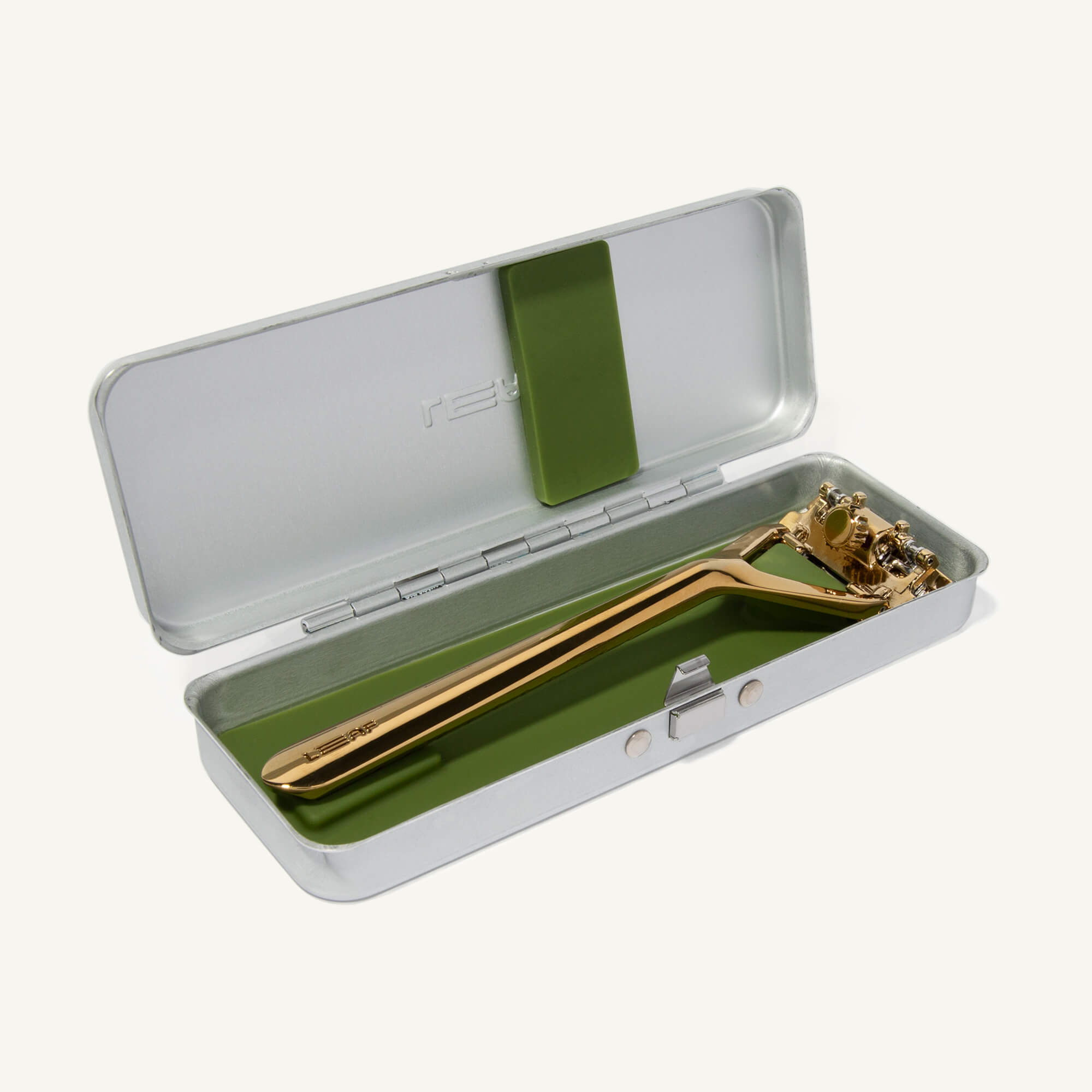 Silver case, open, with green silicone insert and a gold razor laying inside it.