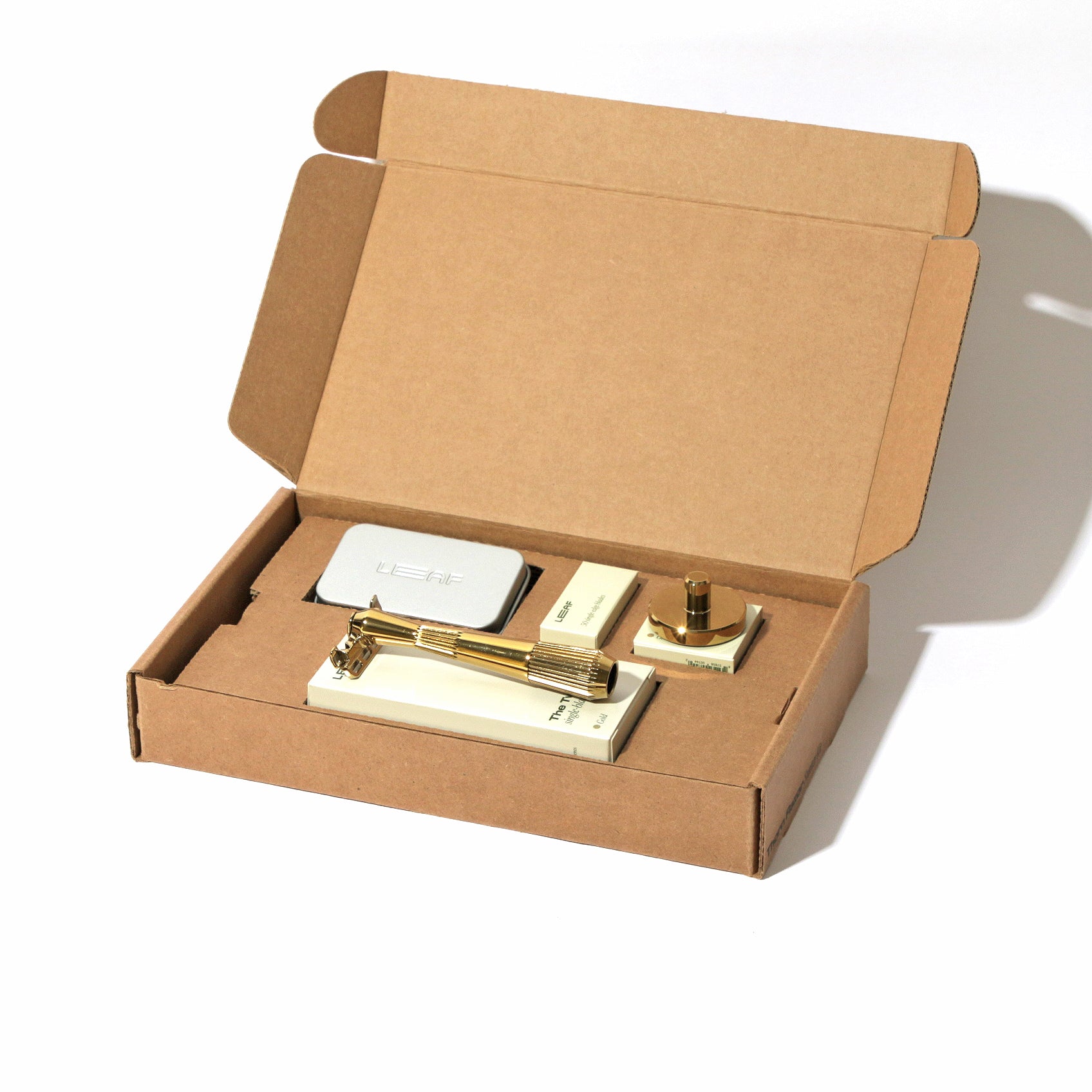 A kraft box on white, open, with a single-edge razor kit displayed in the finish called Gold