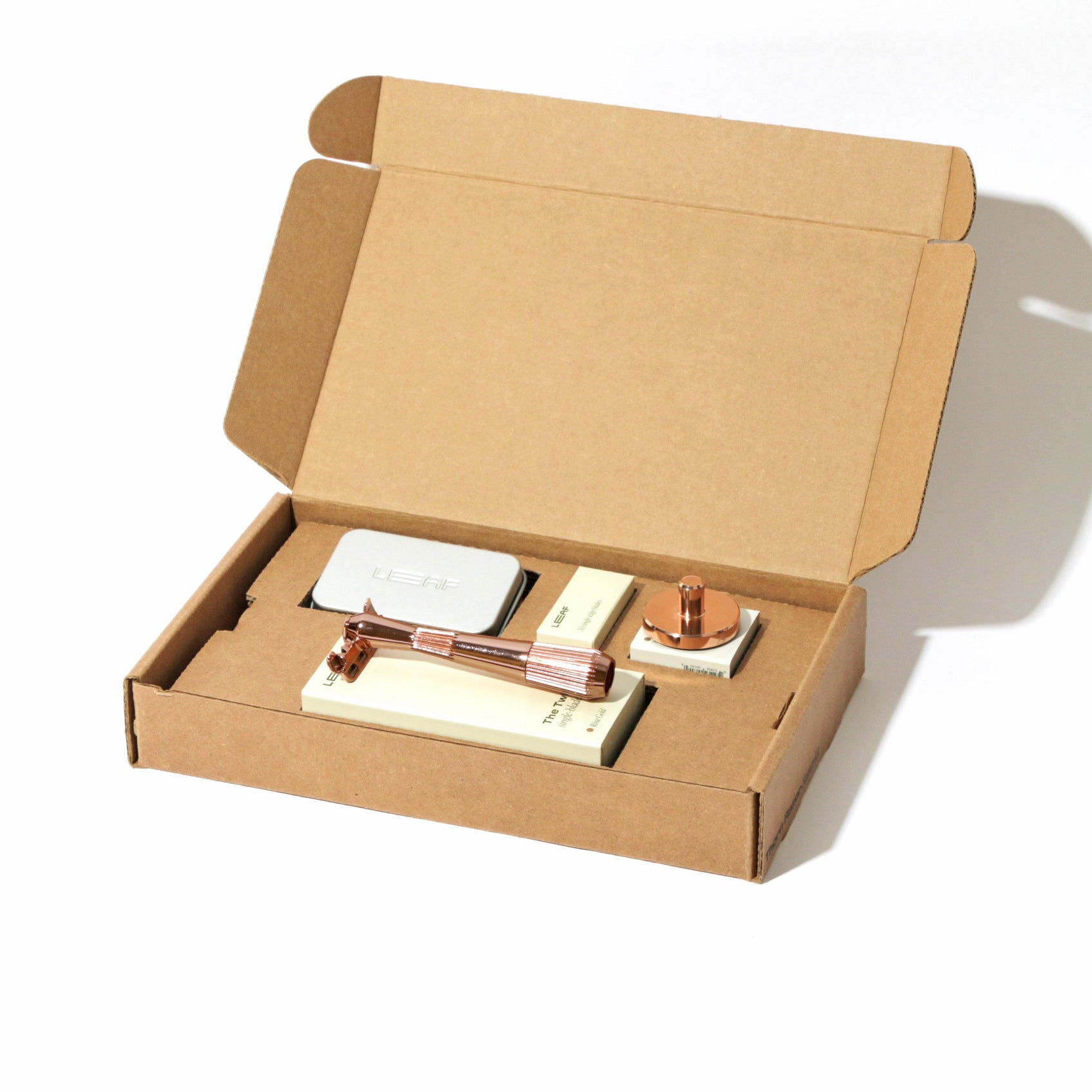 A kraft box on white, open, with a single-edge razor kit displayed in the finish called Rose gold