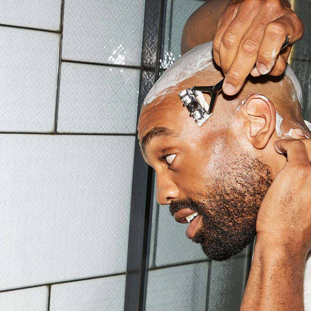 Person shaving their head with a chrome Leaf razor in a bathroom.
